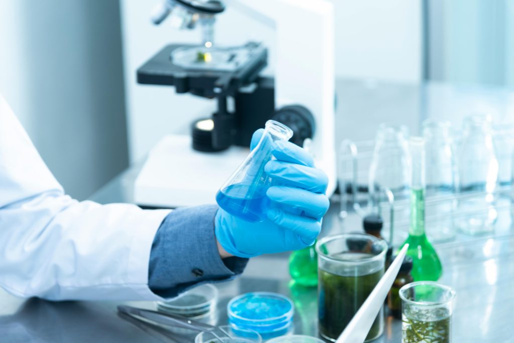 Scientist in blue gloves examining test tube with blue liquid in modern laboratory - self reflection as scientific method for personal growth